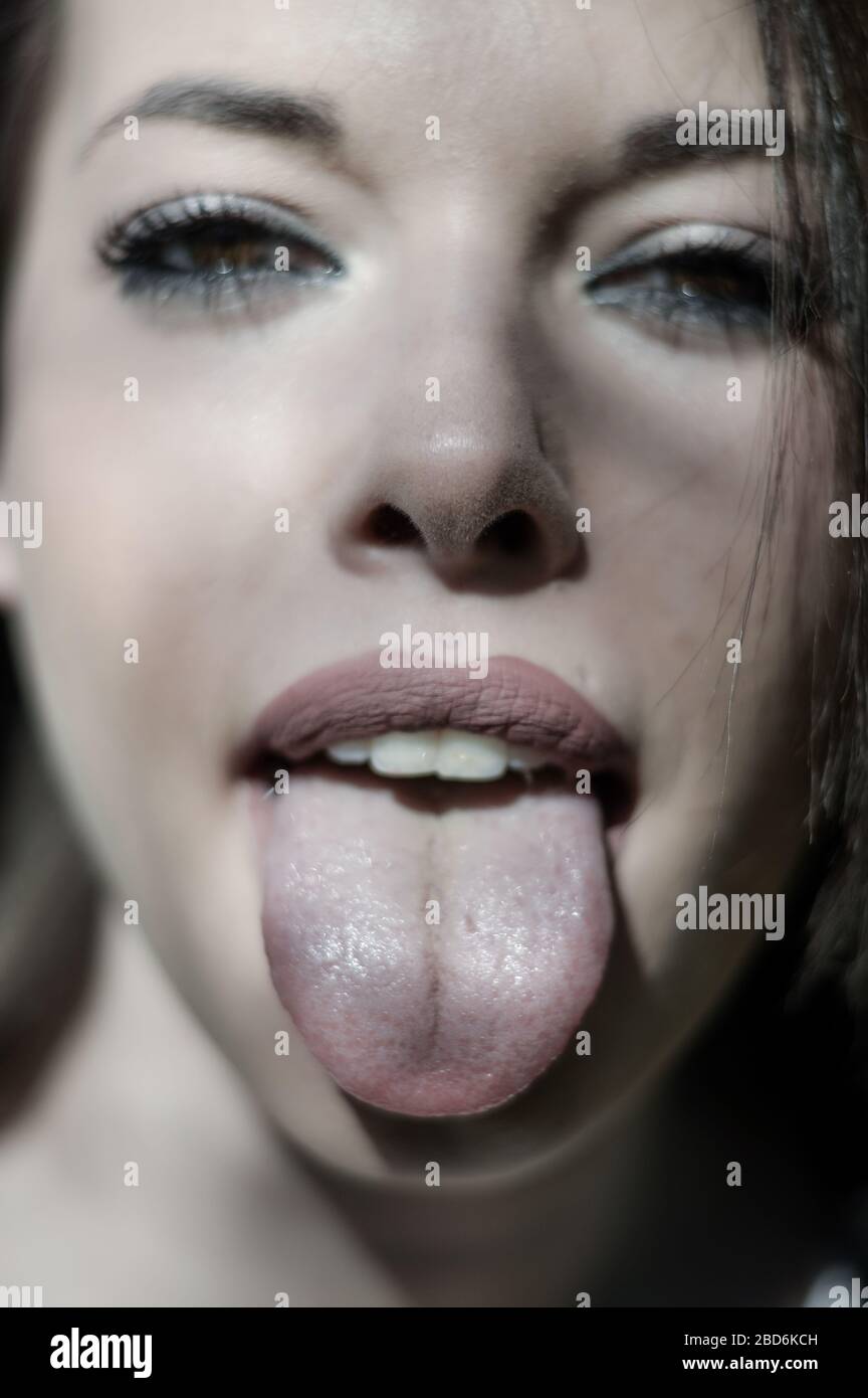 Close up of young woman sticking out tongue. Positive girl having fun outside in a sunny day. Focus on tongue Stock Photo