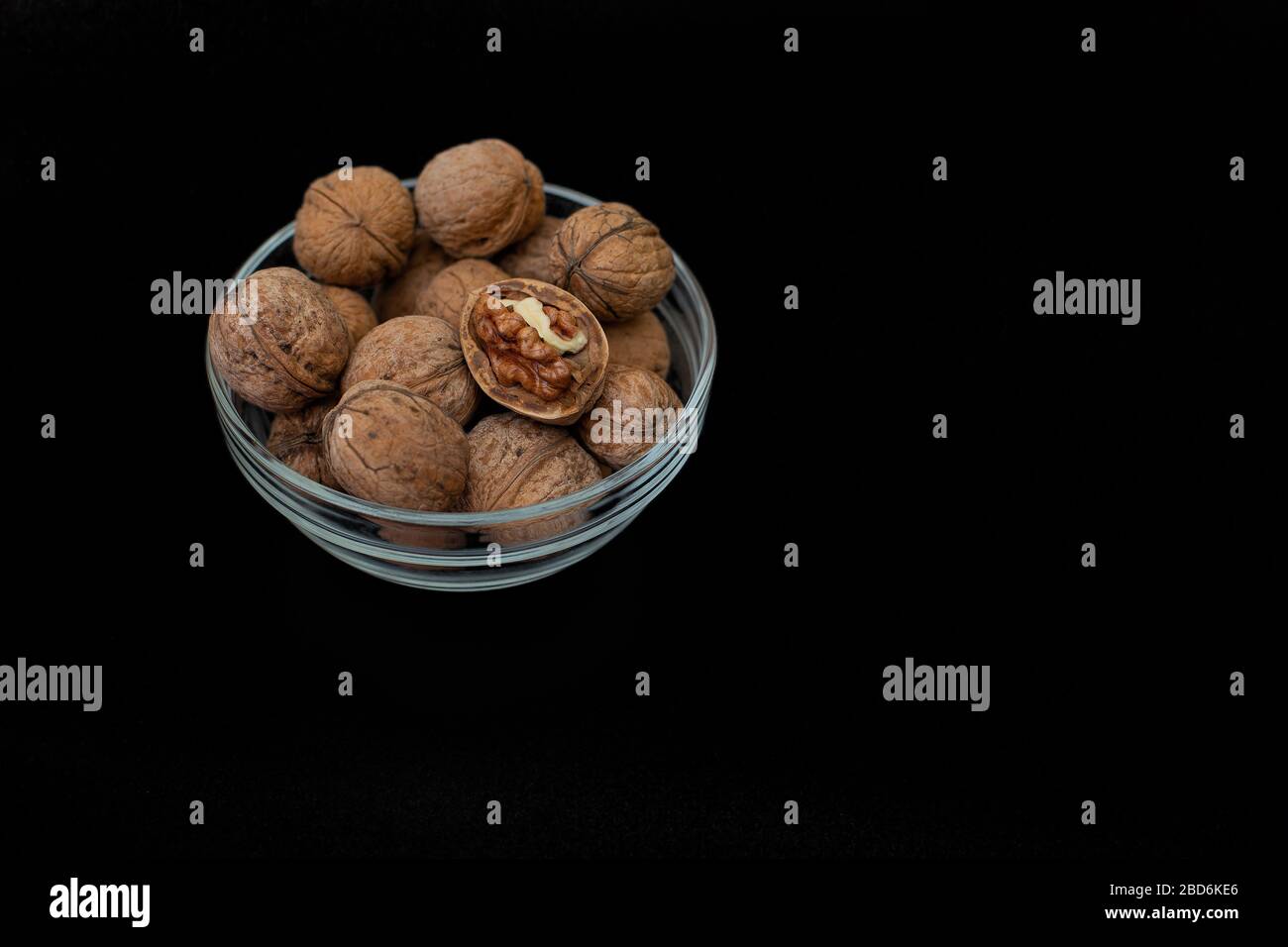 Glass bowl with walnuts in peel on a black background. Copy space. Stock Photo