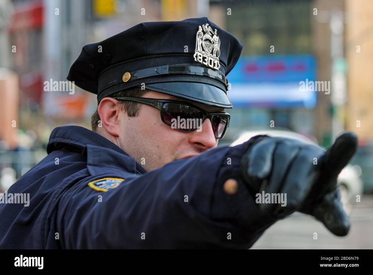 NYPD police officer with sunglasses and peaked cap pointing direction with his leather glove covered hand in Manhattan, New York City, United States Stock Photo