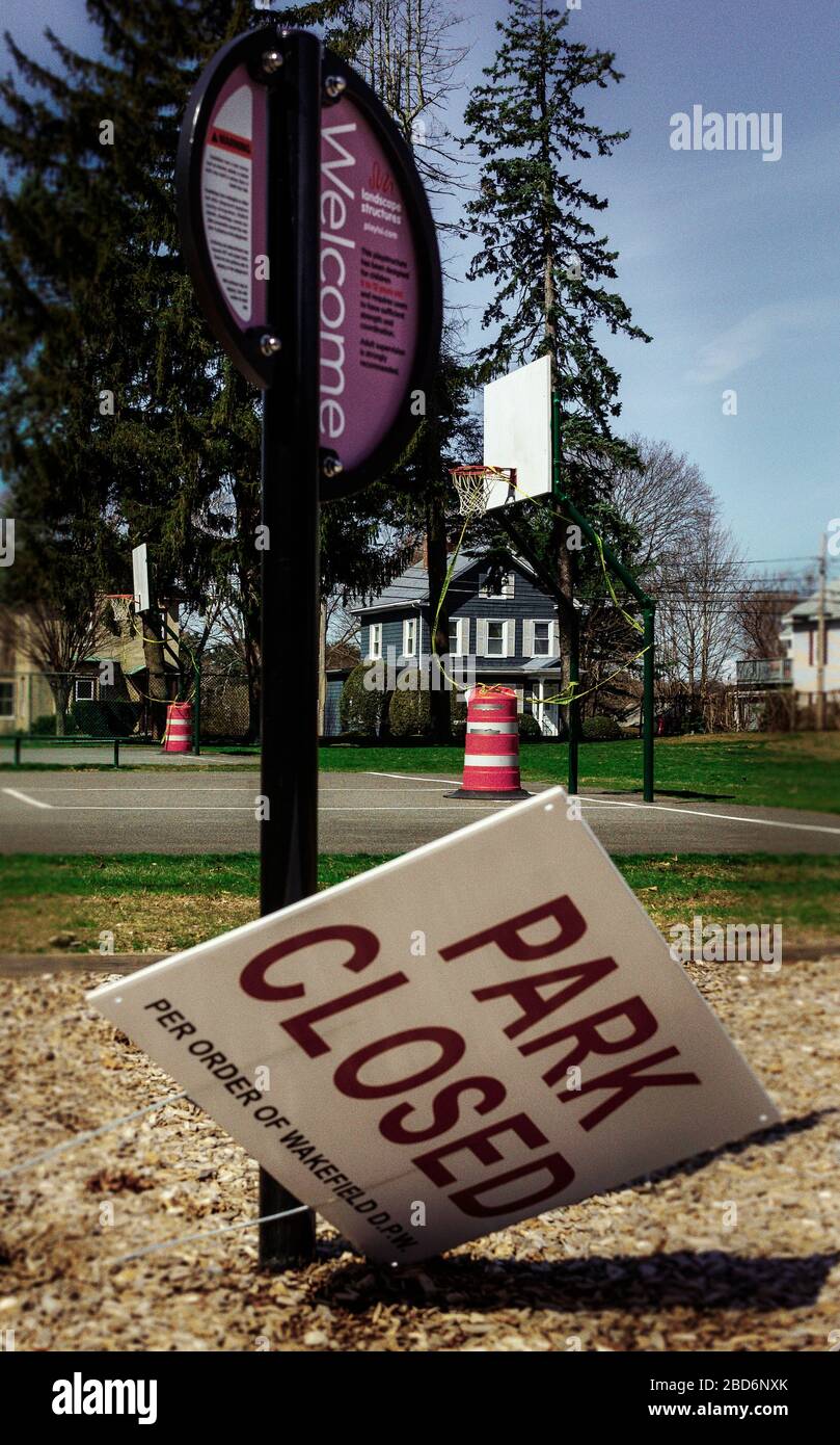 A sign reding Park Closed per order of Wakefield DPW because of COVID-19 (Coronavirus) has fallen over at the base of another sign that welcomes visit Stock Photo