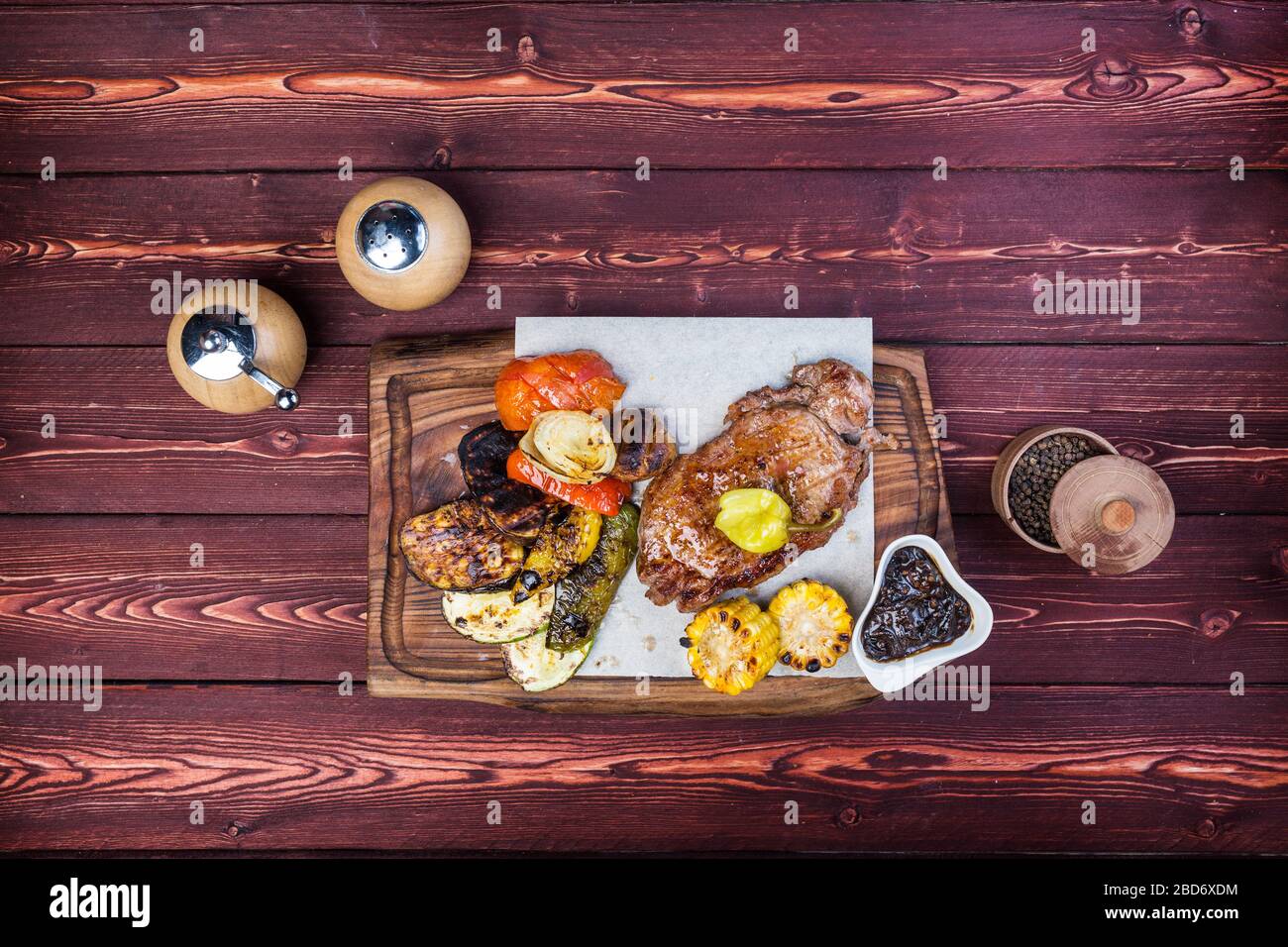 Delicious grilled steak with assorted roast vegetables and corn. There is a pepper grinder and sauce. Top view Stock Photo