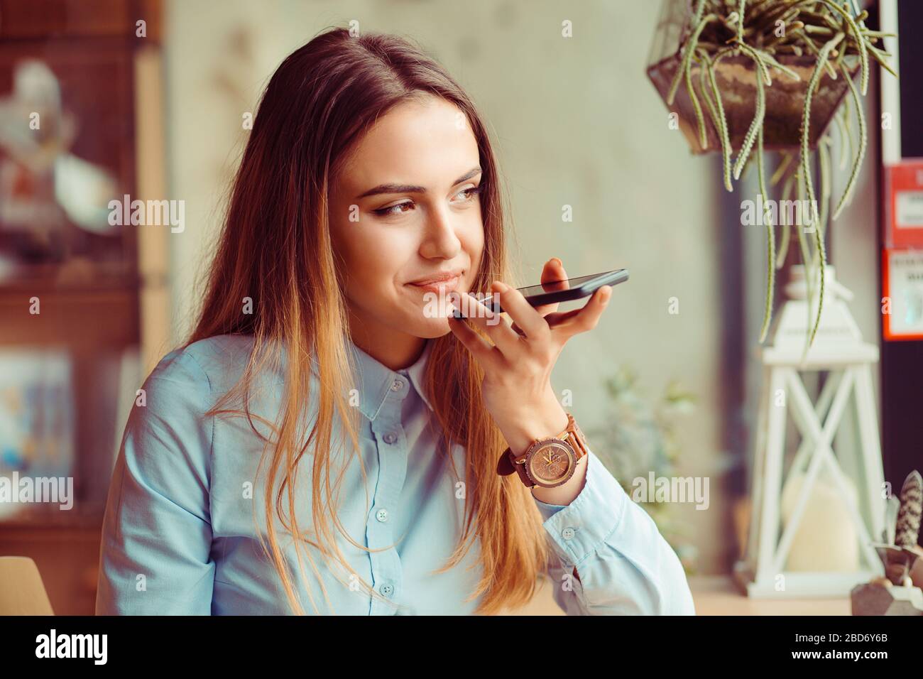 Portrait of a girl using the voice recognition of the phone sitting in a trendy cosy coffee shop cafe in Manhattan New York Stock Photo