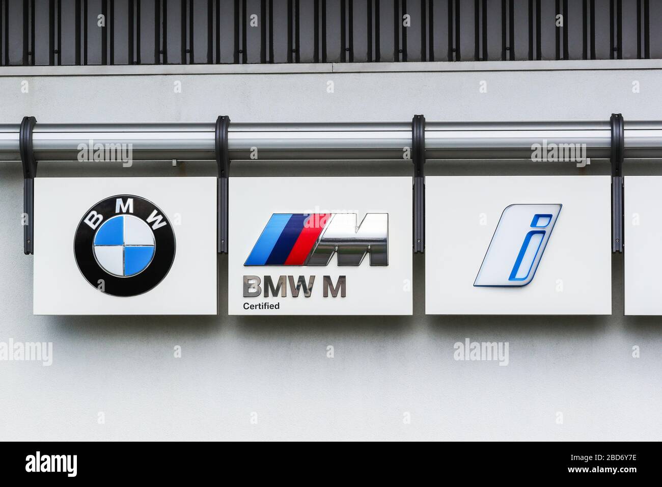 BMW logos showing the standard company logo, the M sport logo and the new electric vehicle 'I' logo, mounted outside a BMW dealership, Ayrshire, UK Stock Photo