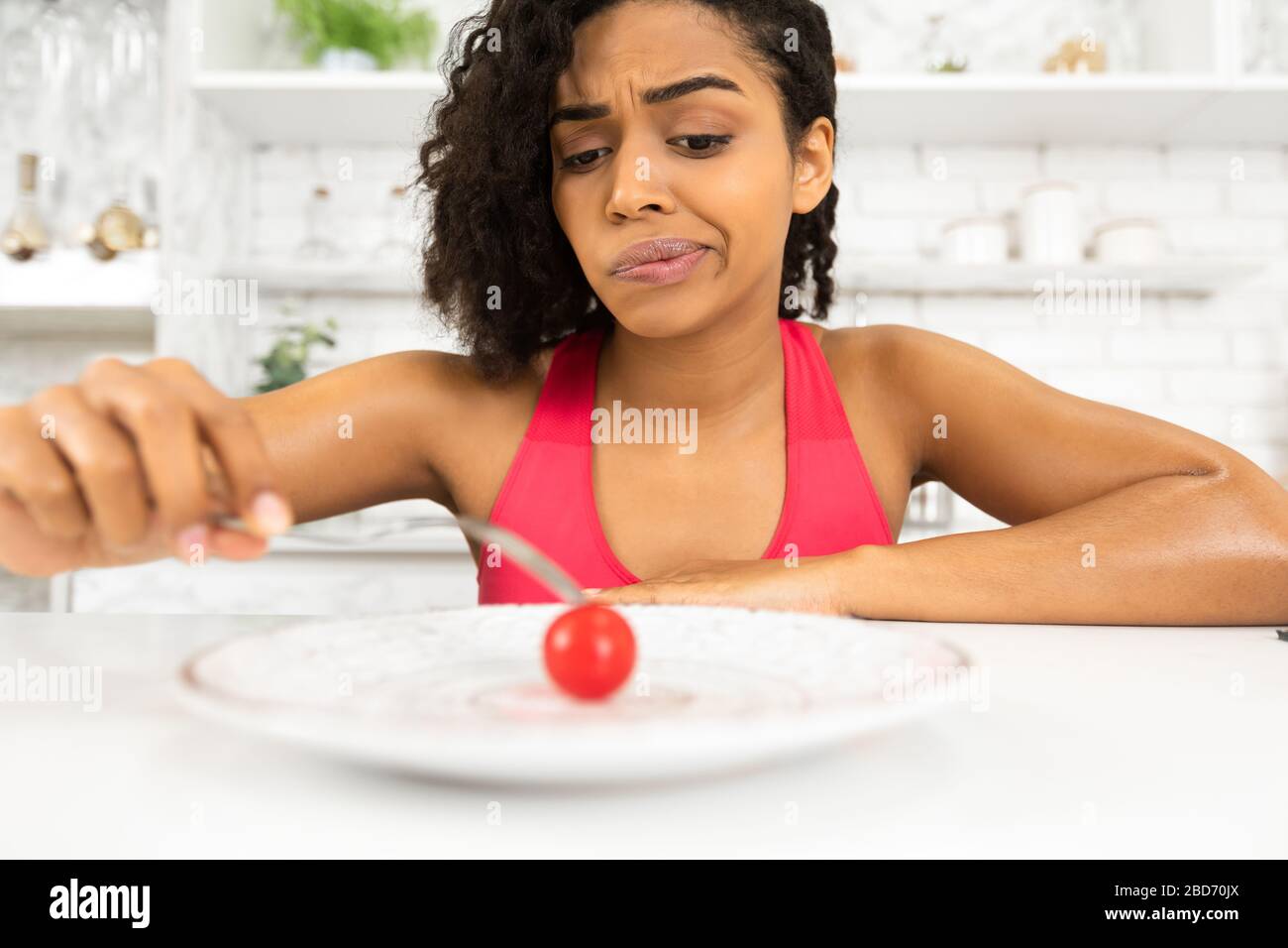 Depressed afro lady looking at tiny tomato on a plate Stock Photo