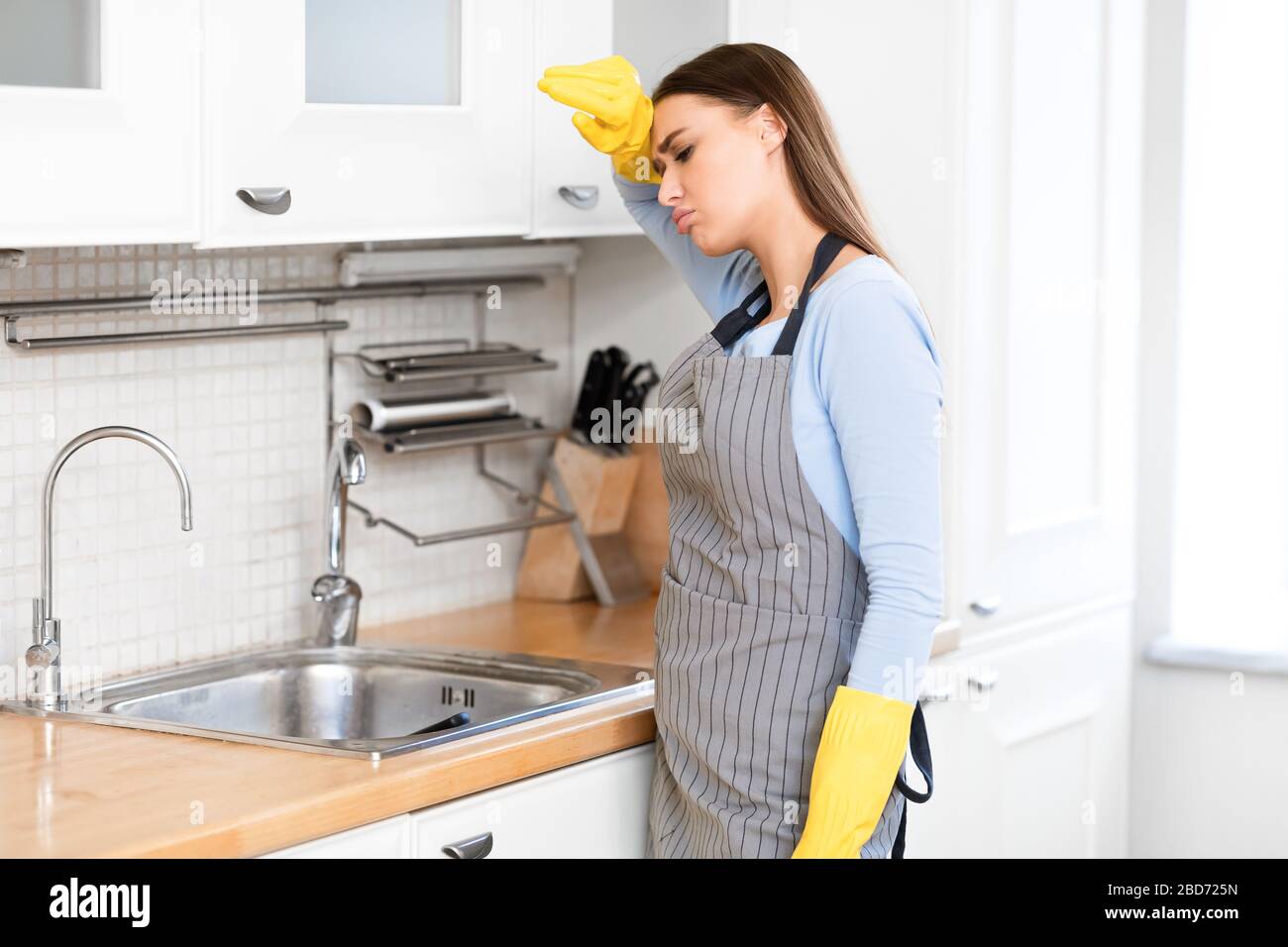 Tired woman wearing yellow rubber gloves after washing dishes Stock Photo