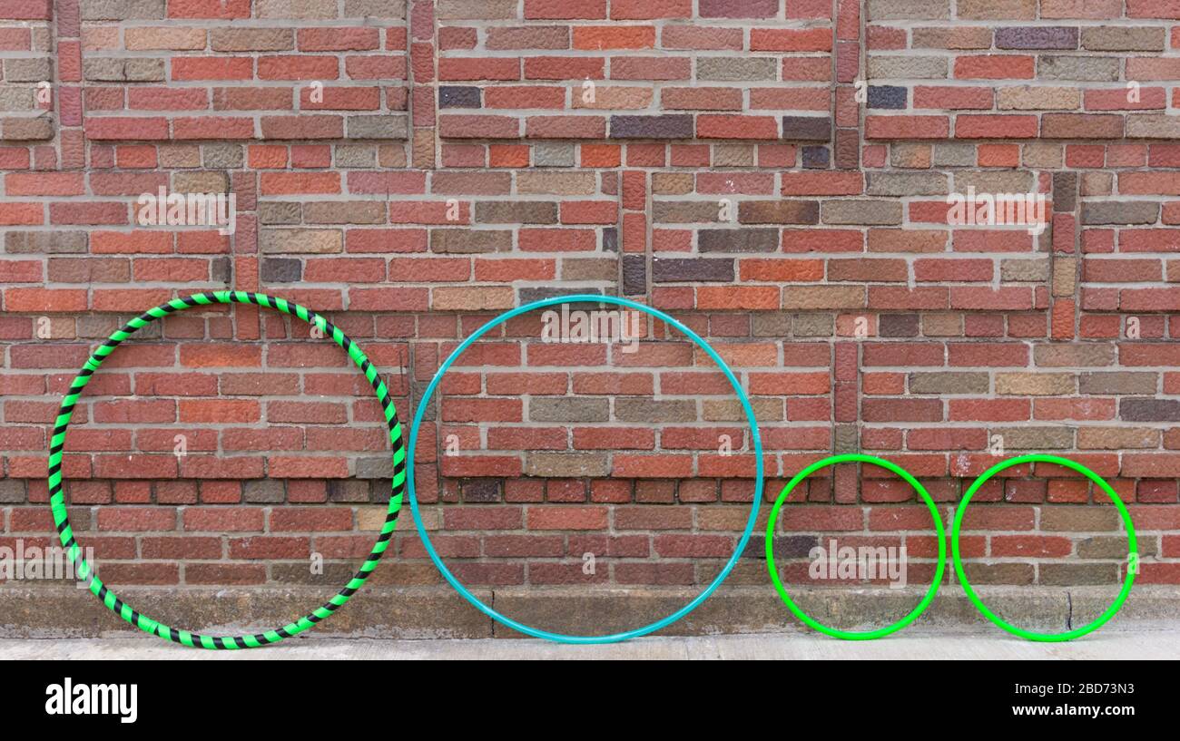 three types of hula hoops lined up against a brick wall, from left to right, a fitness hoop, dance hoop and a pair of mini hoops Stock Photo