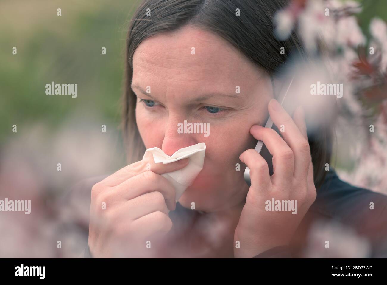 Woman talking on mobile phone and sneezing, springtime tree pollen allergy concept Stock Photo