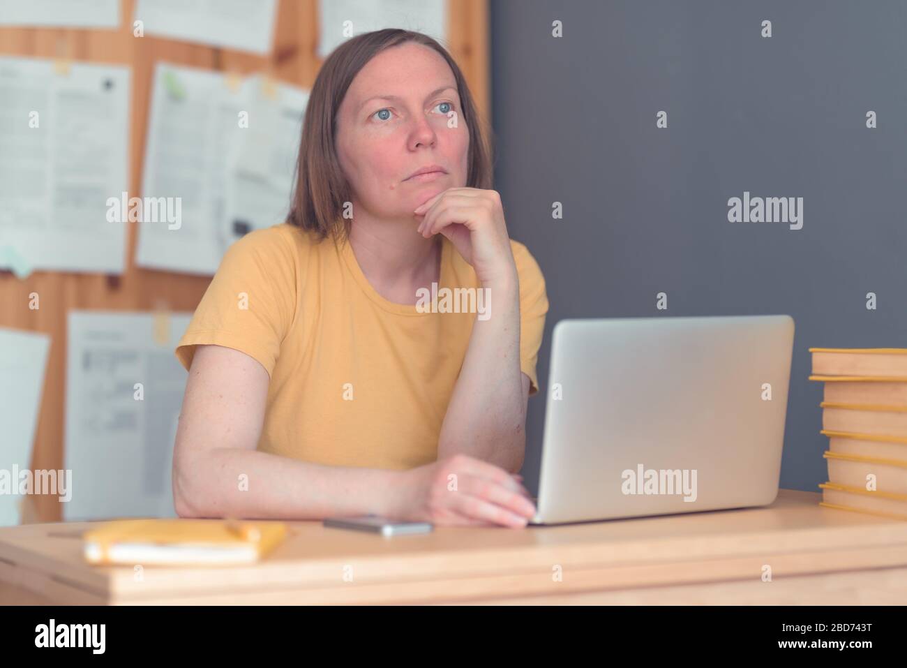 Thoughtful female freelance translator working in home office with laptop computer and smartphone, selective focus Stock Photo