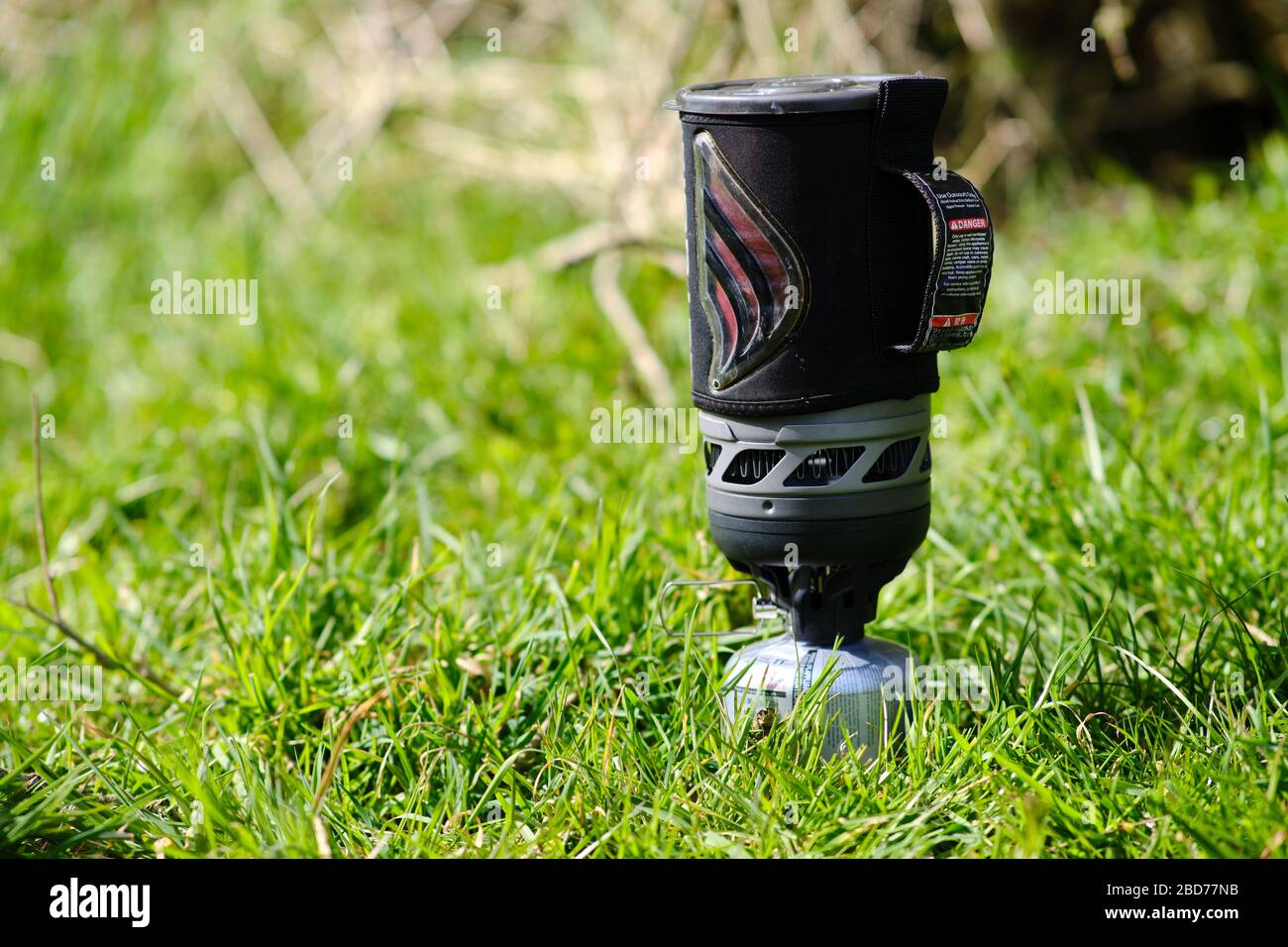 lightweight fast boil gas camping stove being used to boil water in long grass blurred out of focus background Stock Photo