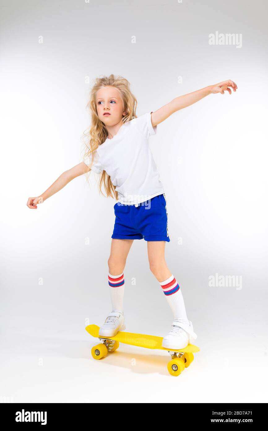 teenager girl in sports shorts rides on a skateboard on a white