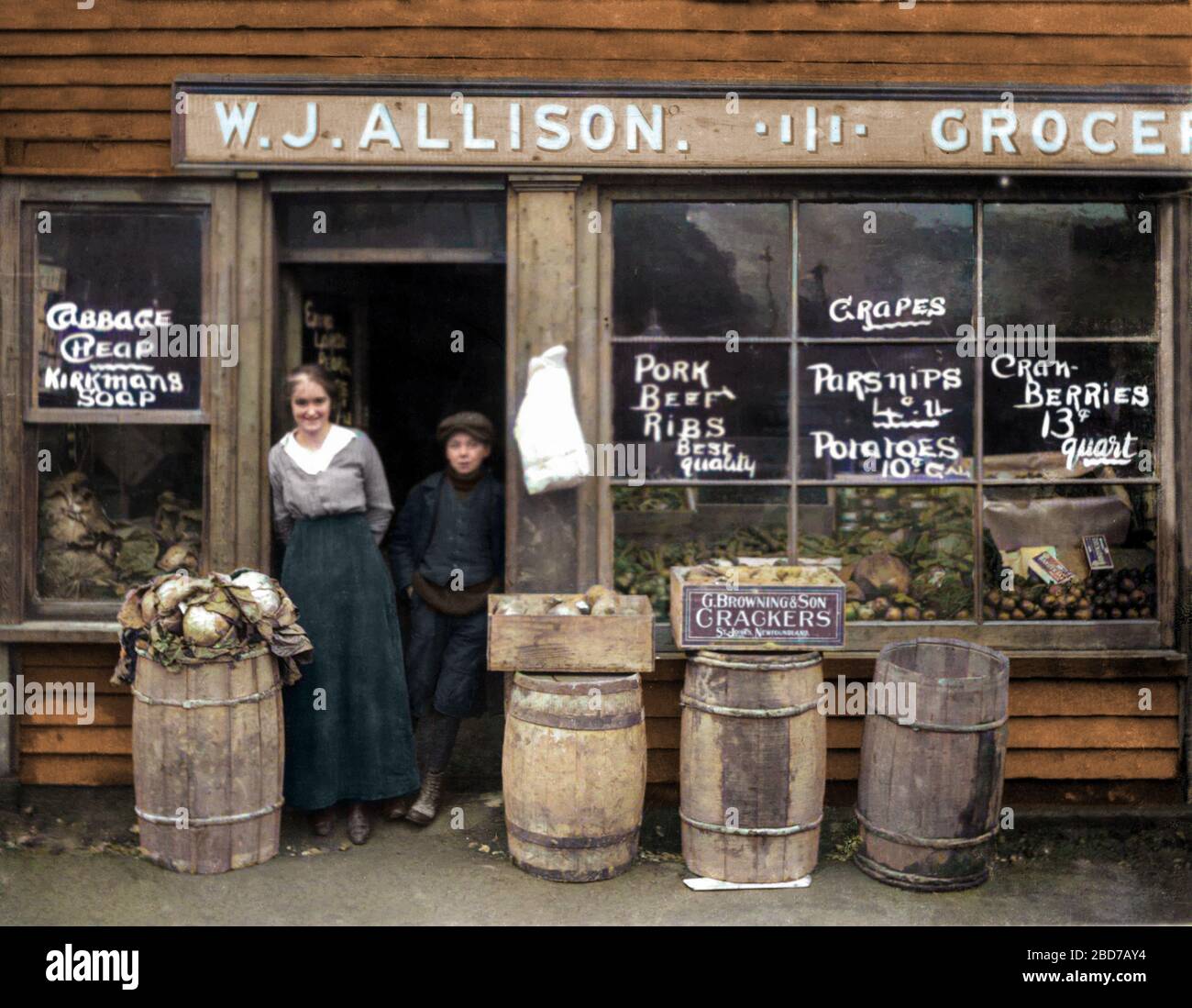 Clerk and delivery boy standing in doorway of W.J. Allison grocery store in St. John's Newfoundland circa 1915. Fruit and vegetables on display. Stock Photo