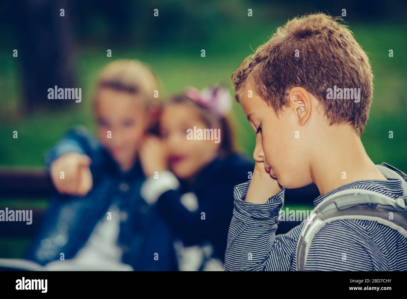 Sad boy feeling left out, teased and bullied by his classmates. Unhappy boy having problems fitting in with others at school. Stock Photo
