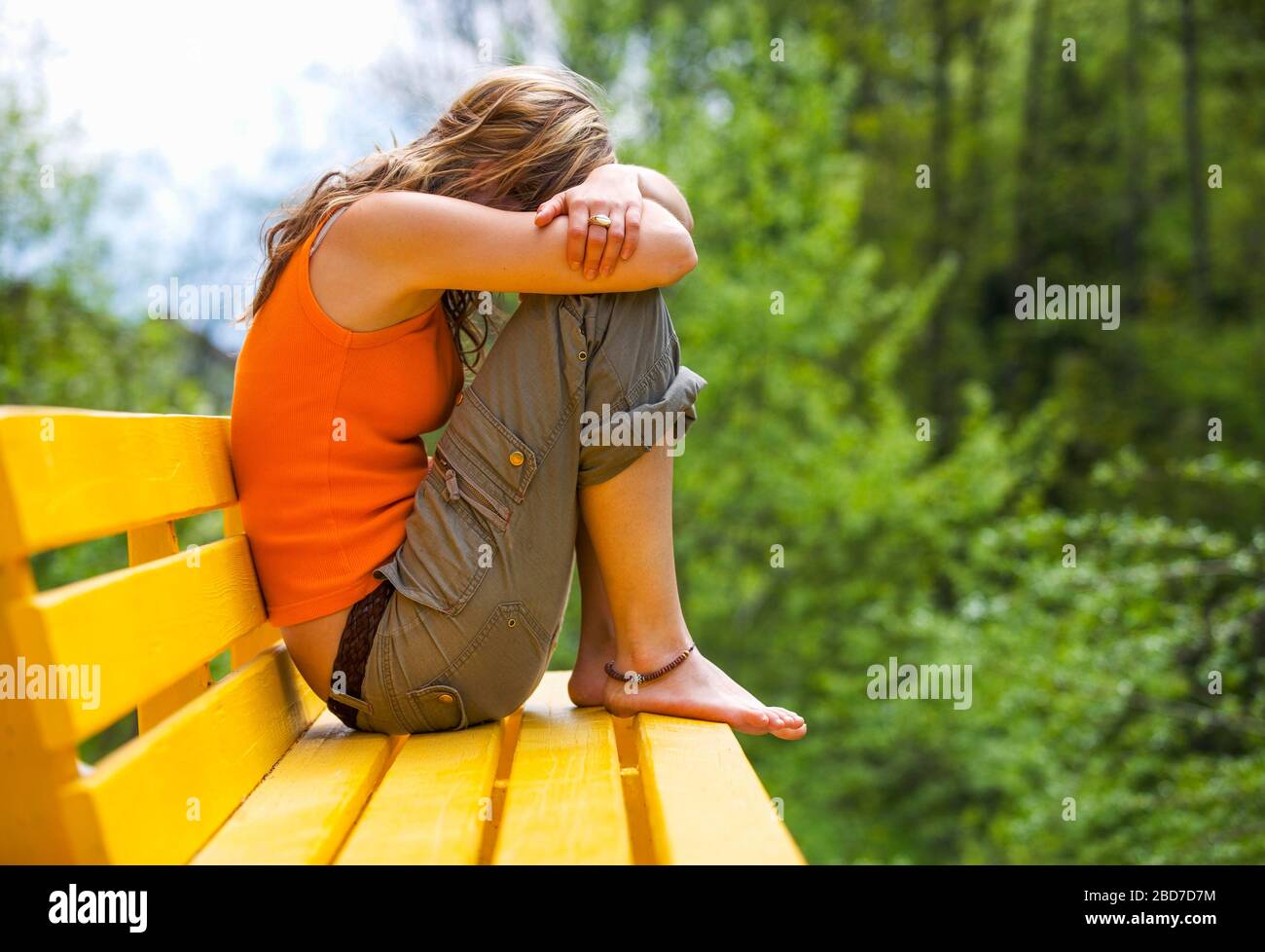 Young woman sitting sad and huddled on a bench, Depression, 22 years, Austria Stock Photo