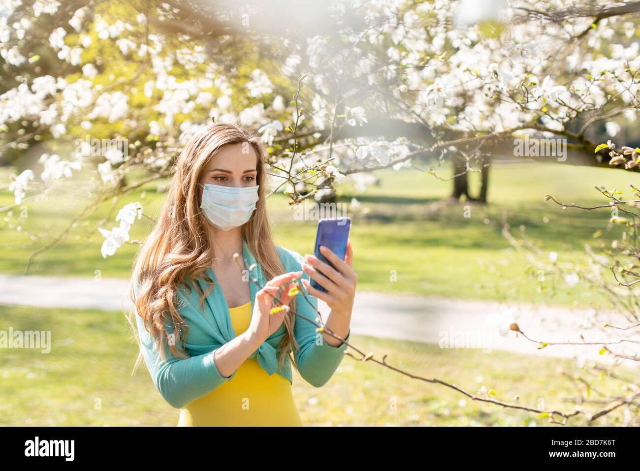 Woman taking a selfie with her phone in spring during Covid-19 crisis wearing a mask Stock Photo