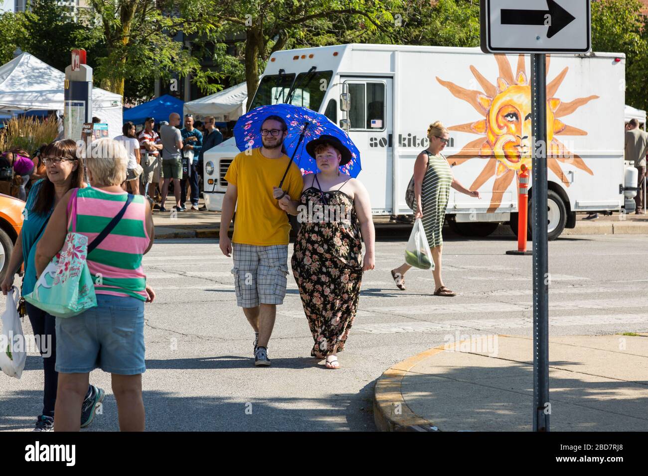 An umbrella protects this couple from the hot sun as they pass the Sol Kitchen food truck at Fort Wayne's Farmers Market in Fort Wayne, Indiana, USA. Stock Photo