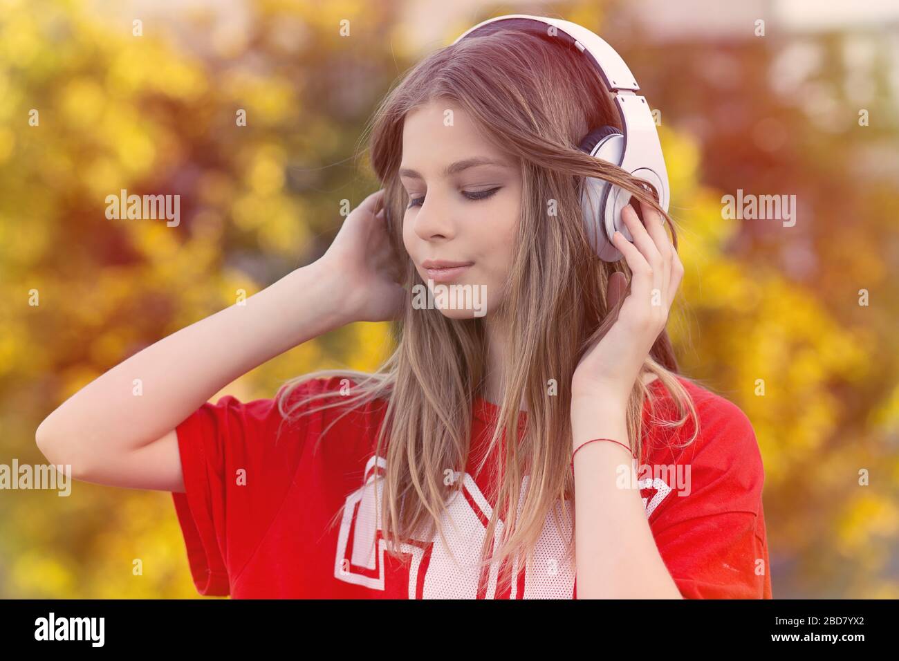 Young happy woman listening to music on headphones standing outdoors on autumn colorful leaves background Stock Photo
