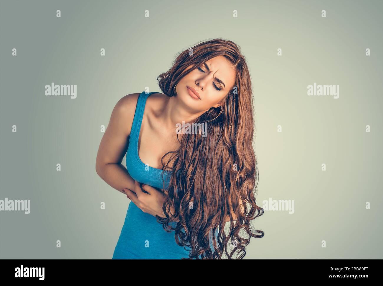 Stomach pain. Portrait young woman hands on stomach having bad aches isolated green wall background. Food poisoning, influenza cramps. Negative human Stock Photo