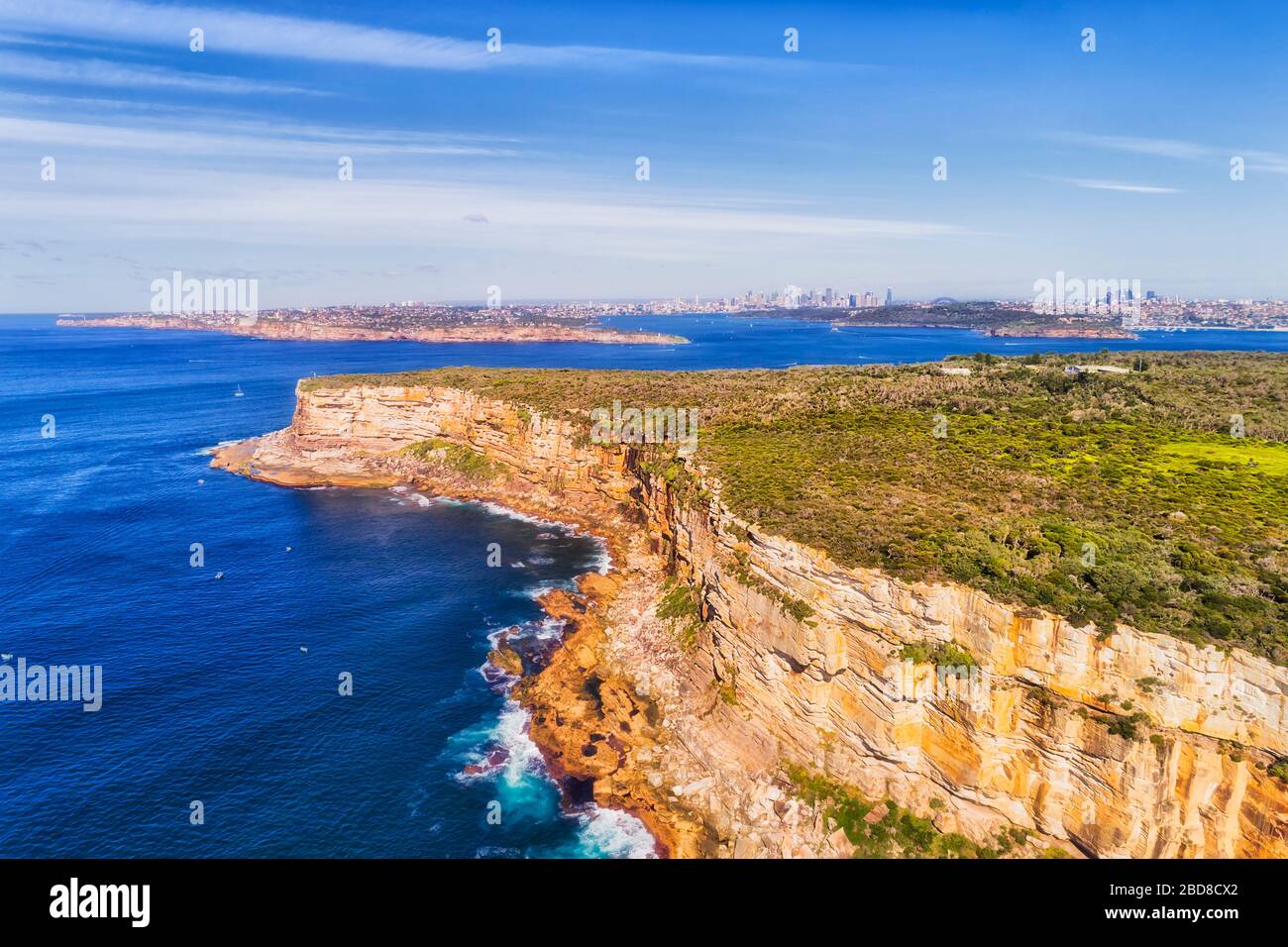 Bright blue pacific ocean and sky over  sandstone heads at the entrance to Sydney harbour in elevated aerial view towaards city CBD. Stock Photo