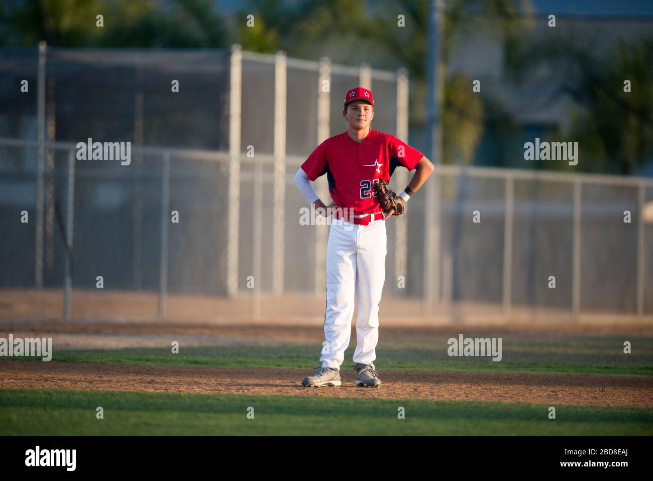 Teen baseball player in red uniform standing in the infield Stock Photo