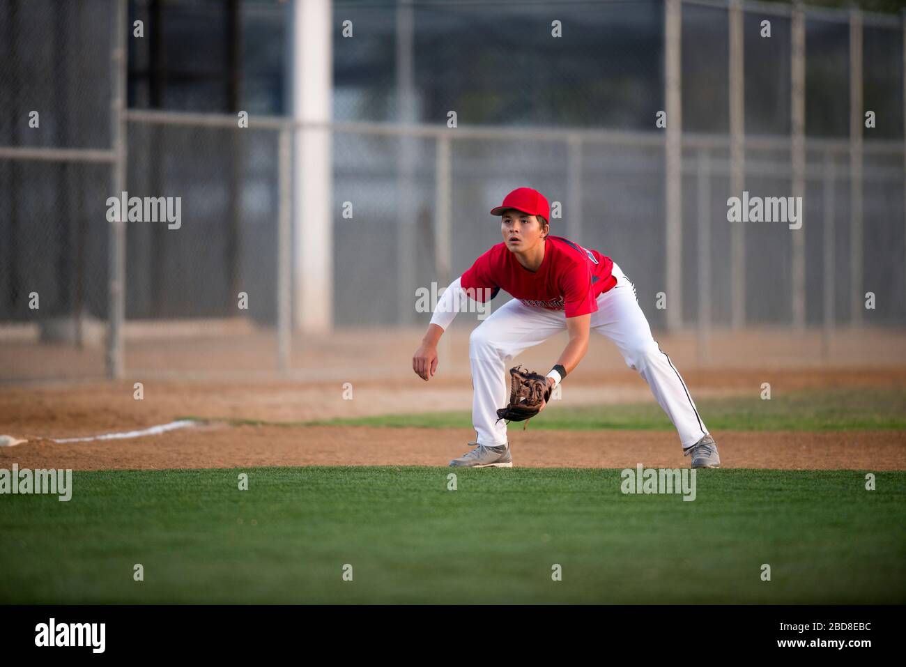 Teen baseball player in red uniform ready for a ground ball Stock Photo