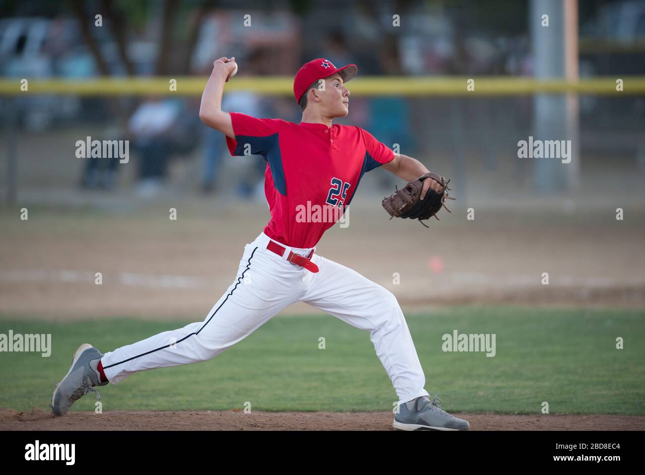 teen baseball player pitcher in red uniform in full wind up on the