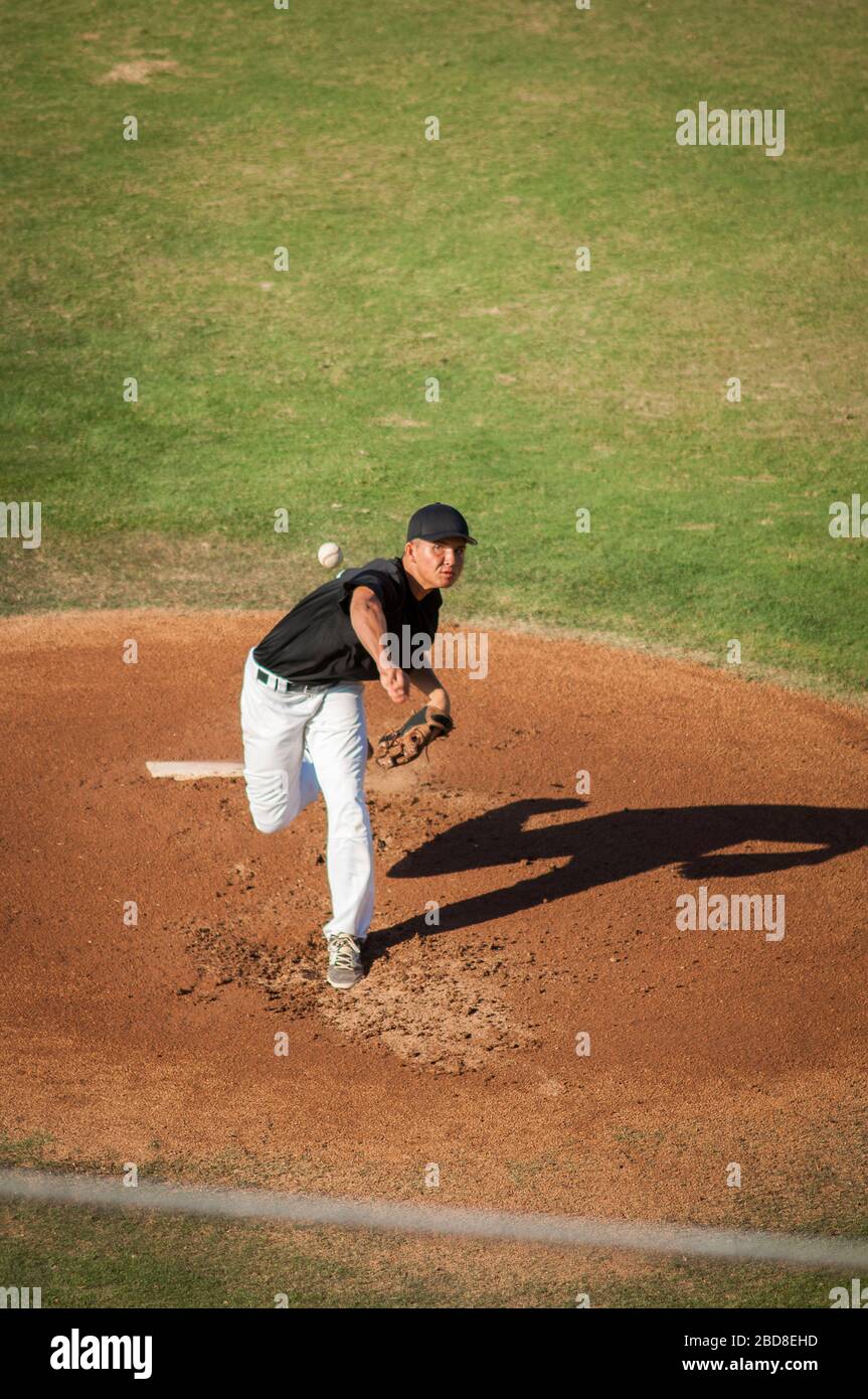 Teen baseball player in black and white uniform pitching Stock Photo