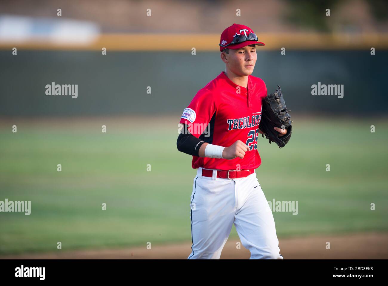 Teen baseball player in red uniform jogging off the field Stock Photo