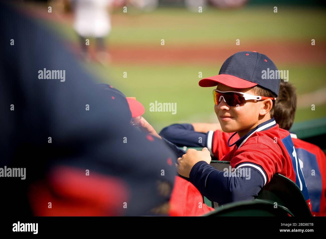 Boy wearing sunglasses and smirking in baseball uniform Stock Photo