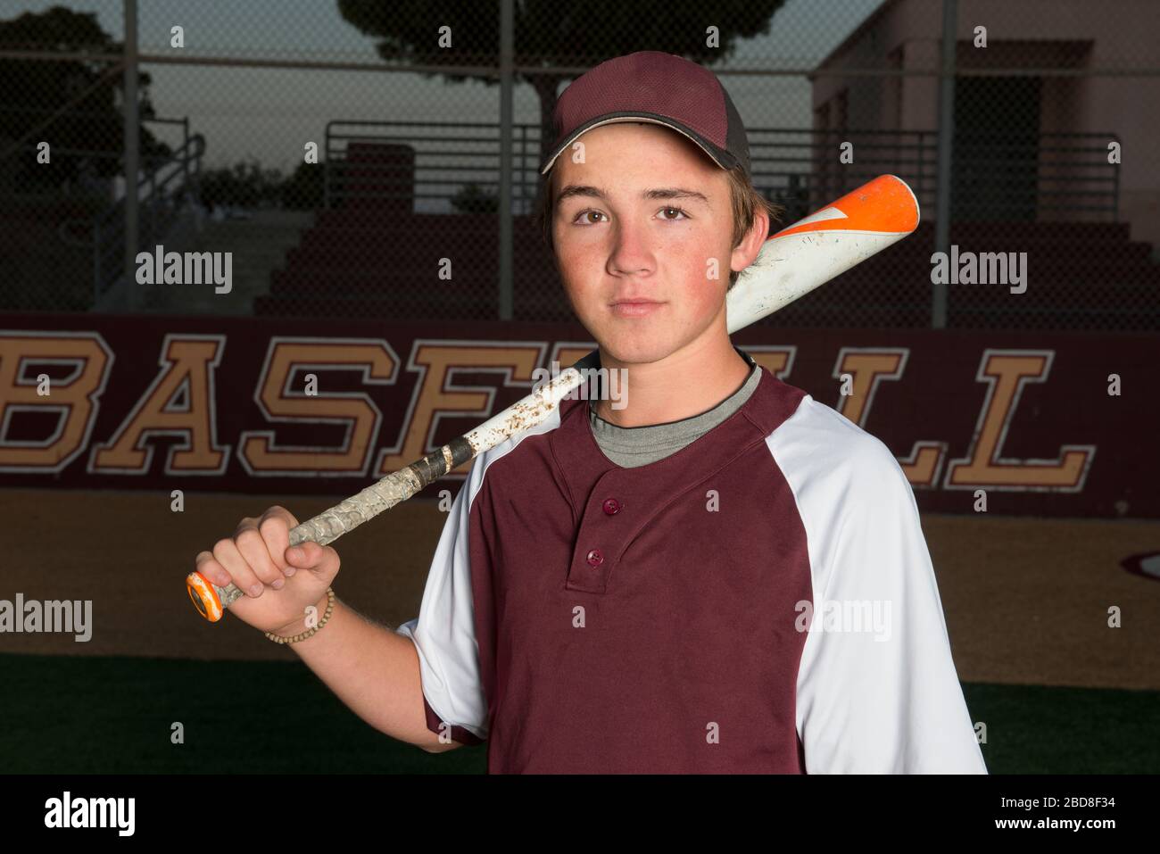 Portrait of a High School baseball player in maroon uniform holding his bat Stock Photo