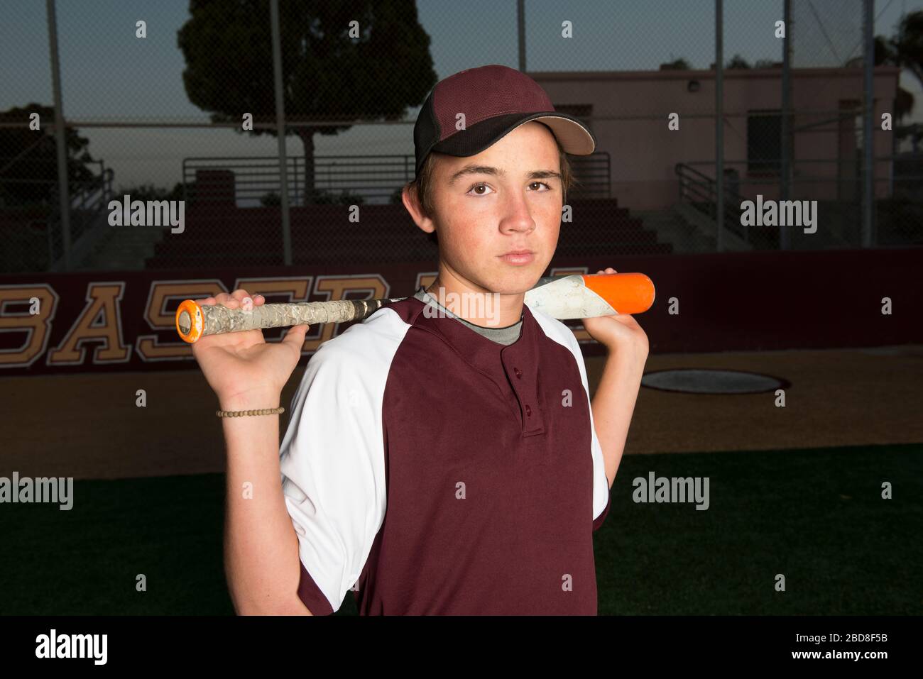 Portrait of a High School baseball player in maroon uniform holding his bat Stock Photo