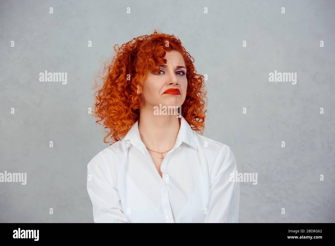 Confused woman. Closeup portrait unhappy young red head curly girl person shrugging shoulders I don't know concept on gray background. Negative human Stock Photo