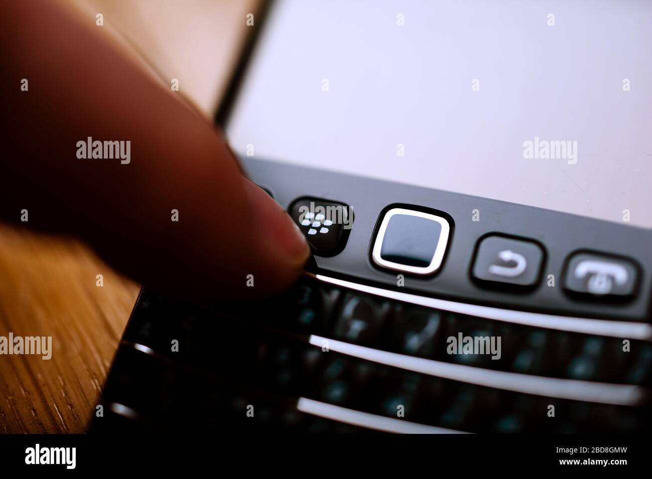 London, United Kingdom - April 21, 2013: Man hand pressing the Blackberry RIM smartphone home button on the vintage smartphone telephone with full qwerty keyboard Stock Photo