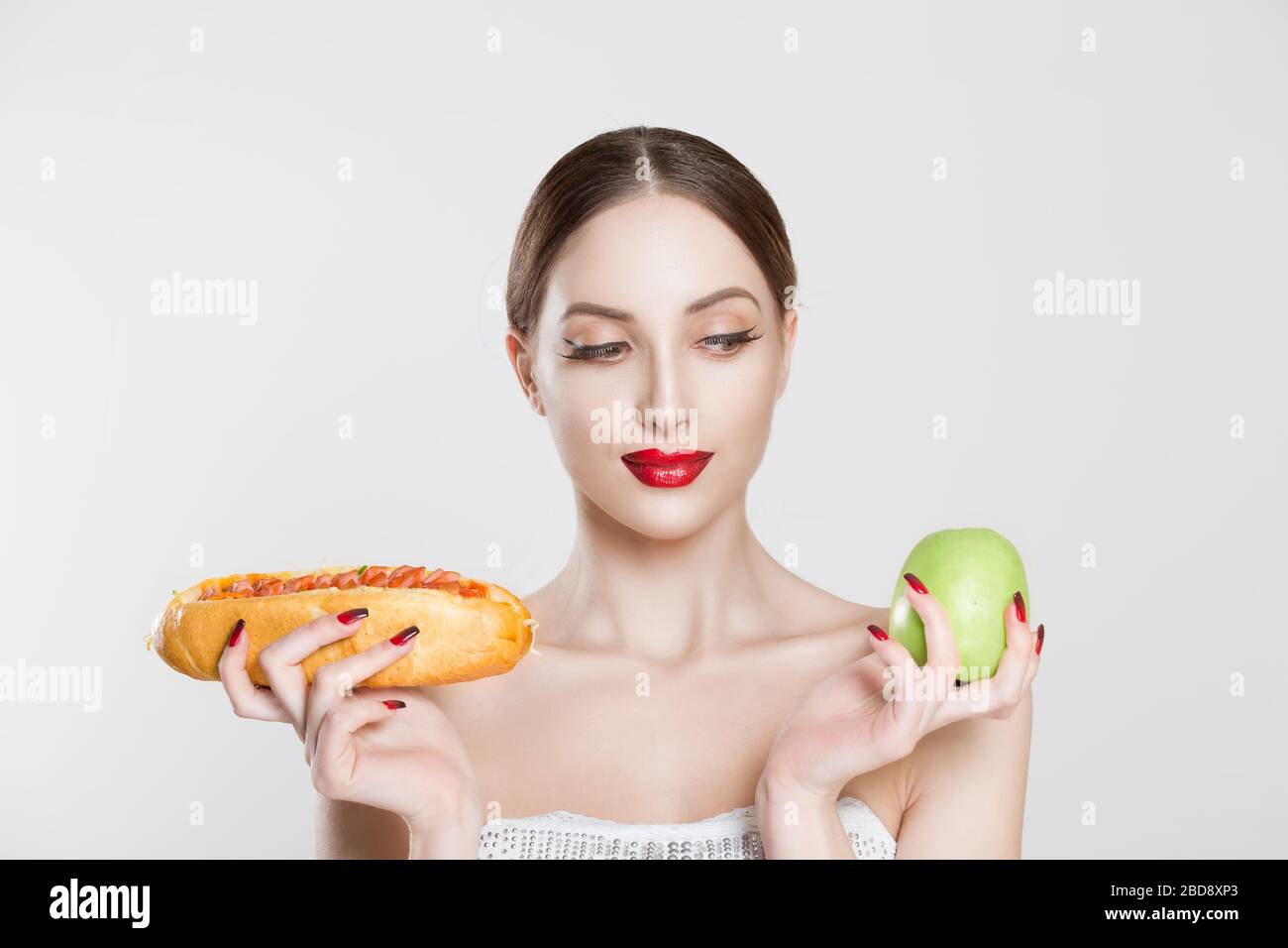 Woman compare tasty unhealthy burger sandwich hotdog in hand and green apple getting ready to eat healthy food isolated on a white background, healthy Stock Photo