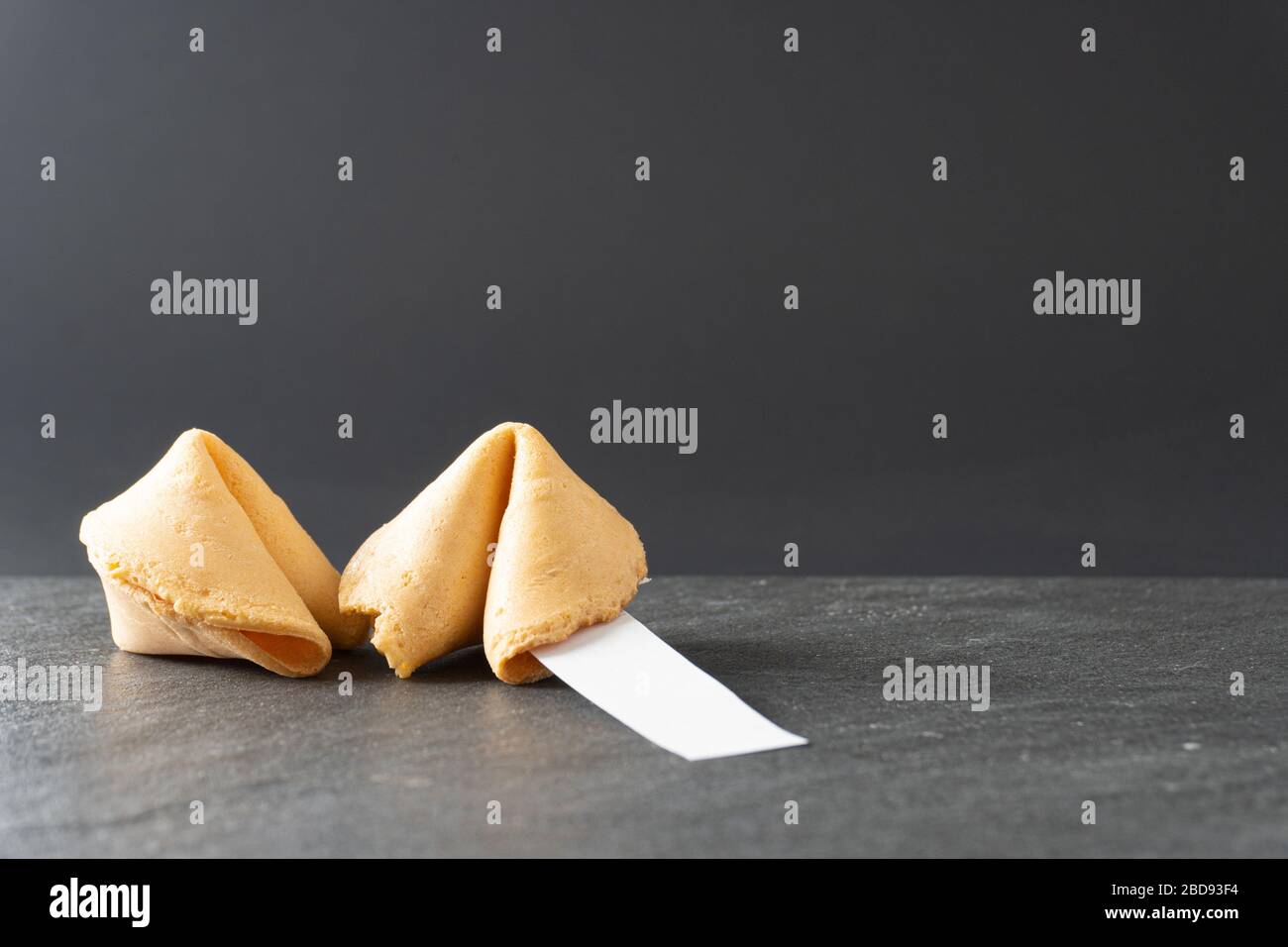 Two fortune cookies rest on a black slate table top with a blank fortune and copy space; landscape view Stock Photo