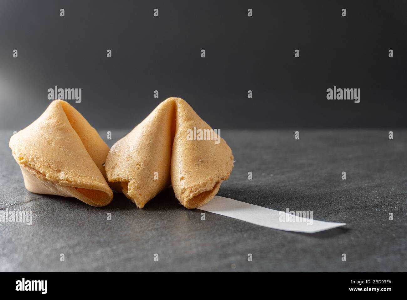 Close-up of two fortune cookies with a blank fortune coming out of it on a black slate background; landscape view Stock Photo
