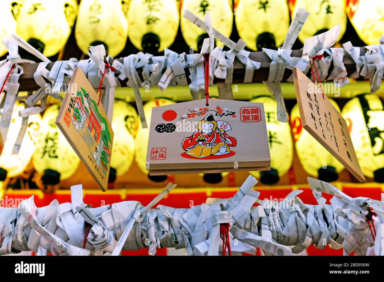 Wooden Ema plaques hang at a shrine in Japan during the 2016 New Years, the year of the fire monkey, while illuminated by washi paper lanterns. Stock Photo