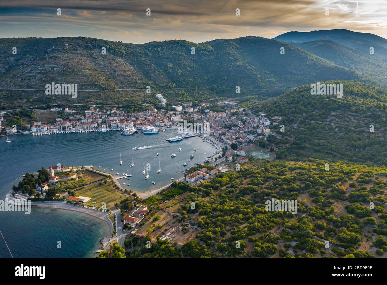 Aerial view of marina Vis at sunset, Croatia, a lot of chaotically standing boats in a bay, roofs of orange color, sunshine, hills with green trees Stock Photo