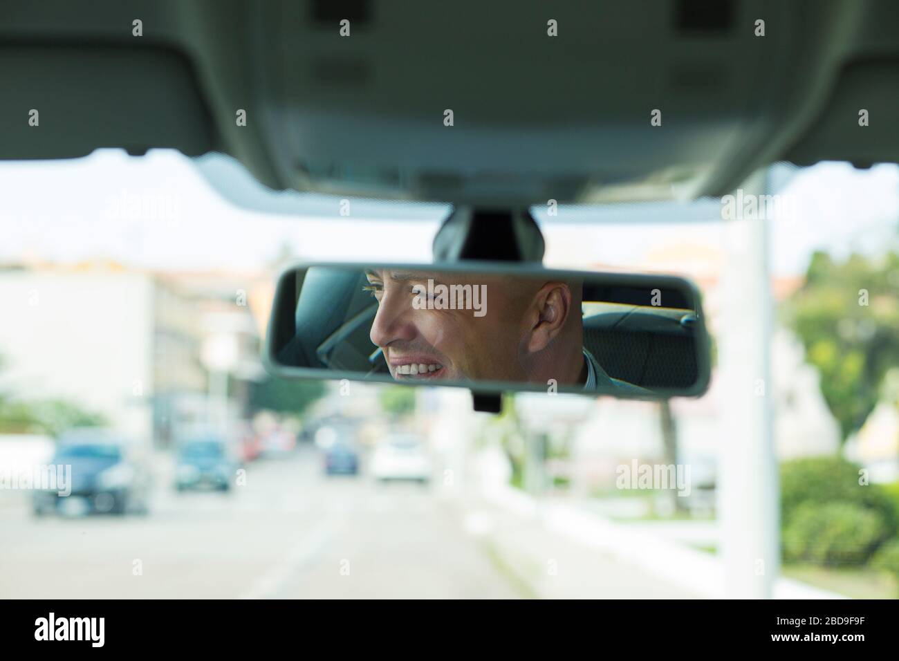 Closeup portrait, happy young man driver looking at rear view mirror ...