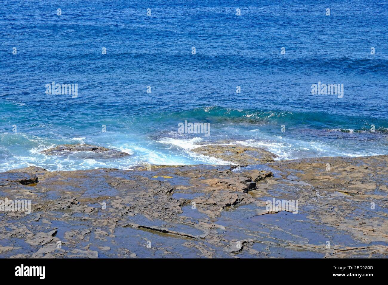 Looking down at a  rock platform, or shelf, and the sea with small waves rolling in. Stock Photo