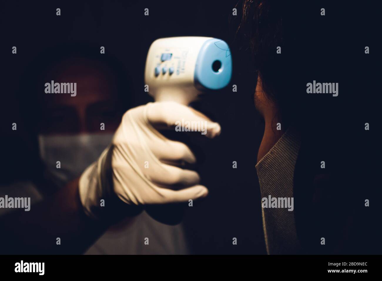 Senior healthcare worker measuring a young adults body temperature with