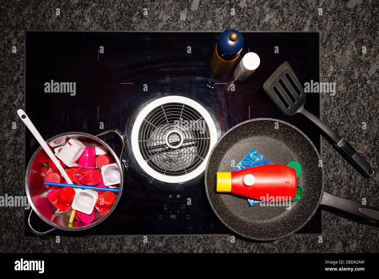 Concept of food pollution with plastic waste. Top view of a stove with a frying and a cooking pan filled with plastic objects representing food. Stock Photo