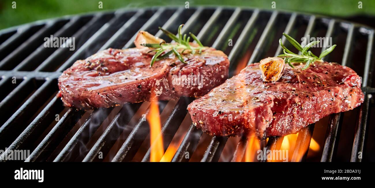 Succulent slices of raw beef steak on a BBQ grilling over the flaming coals in a close up low angle outdoor panorama banner Stock Photo