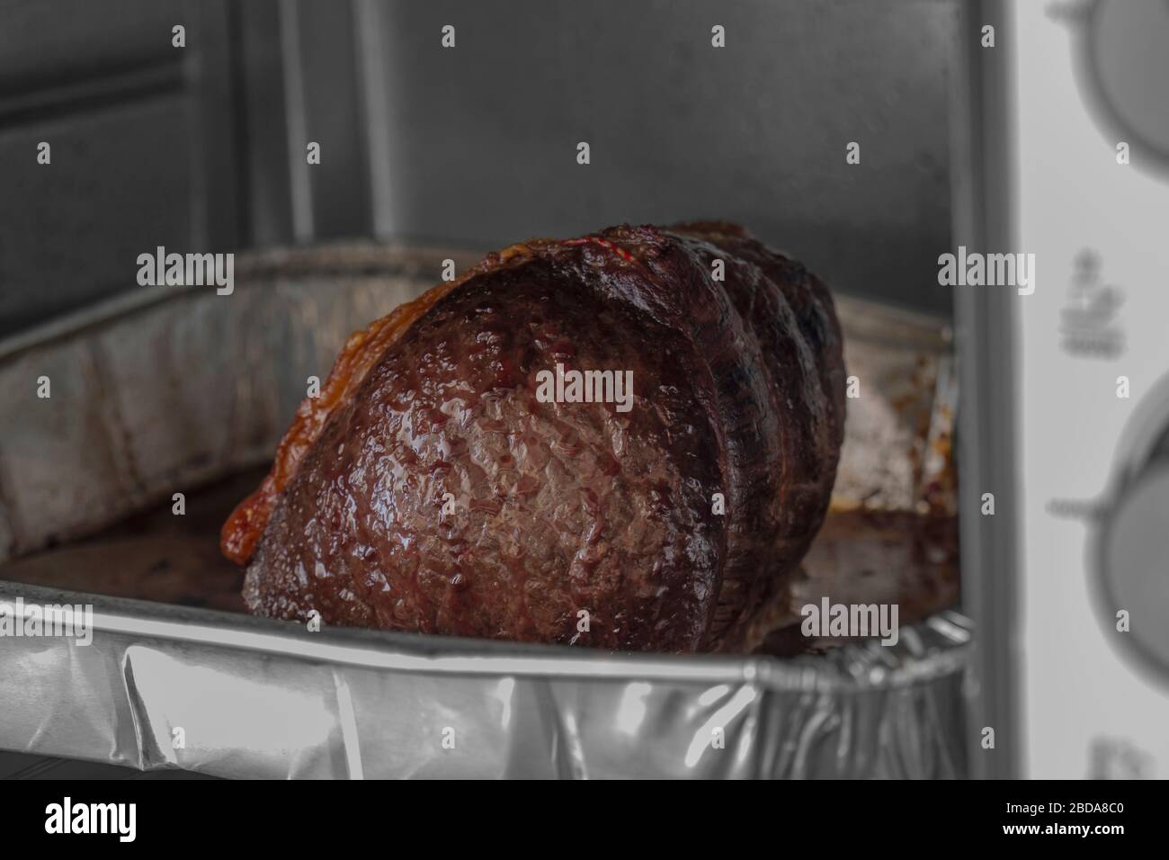 Beef topside joint cooking in a foil baking tray in an electric oven