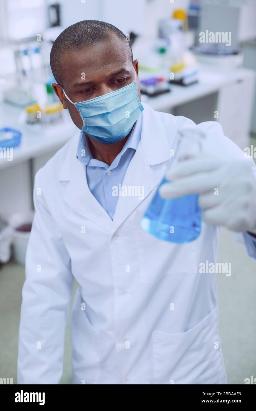 Concentrated male researcher looking at the flask Stock Photo
