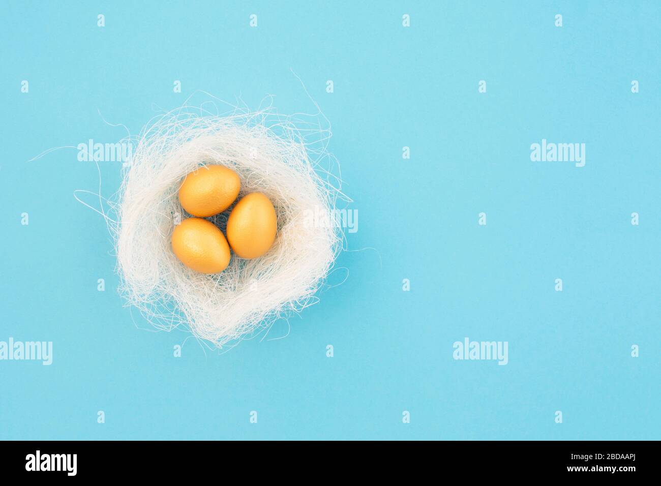 Decorative bird nest with golden easter eggs on blue pastel background. Easter concept. Flat lay. Stock Photo