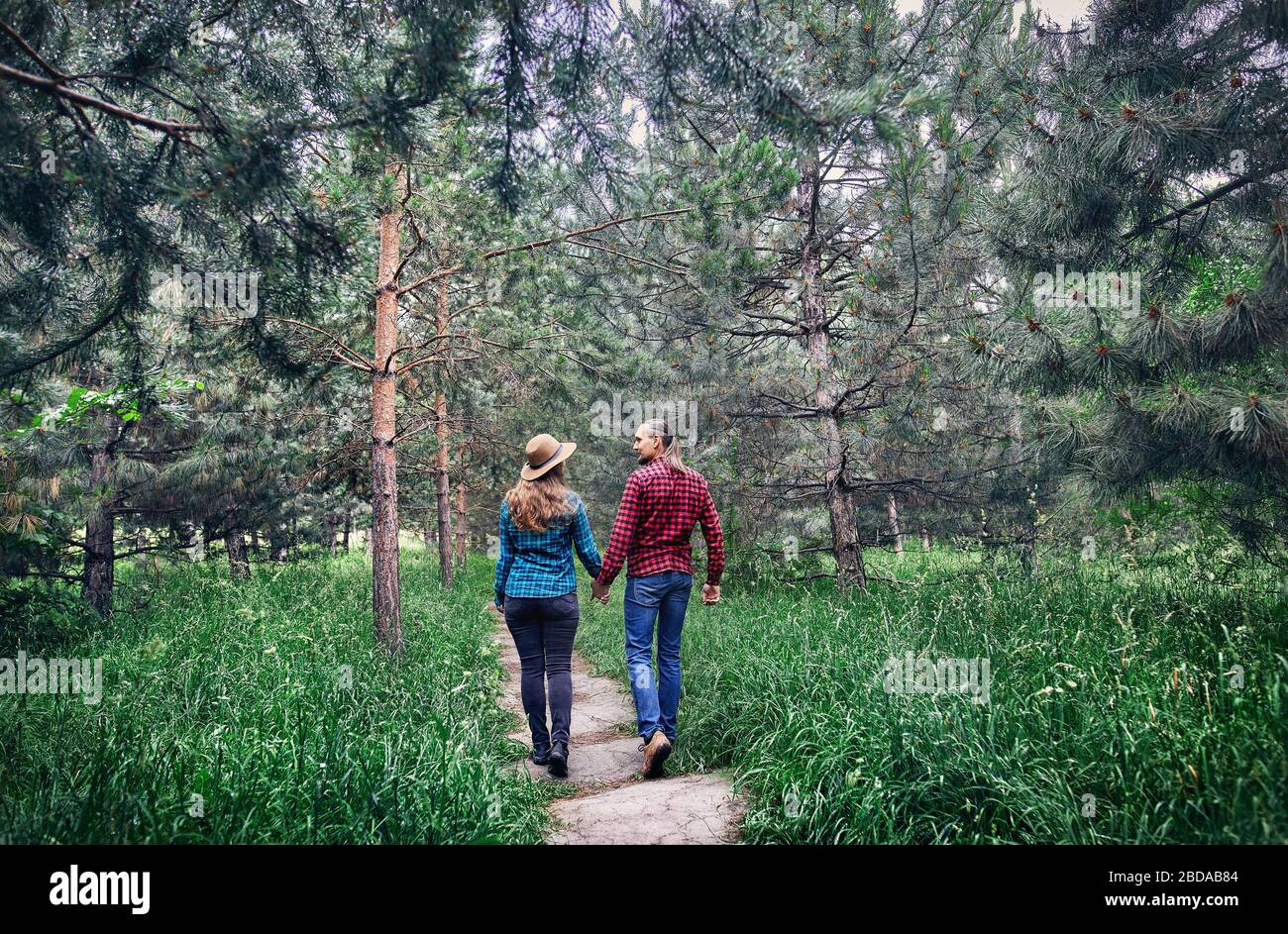 Young hipster couple in checkered shirt holding by hands and walking in the pine tree forest. Love in the nature. Stock Photo