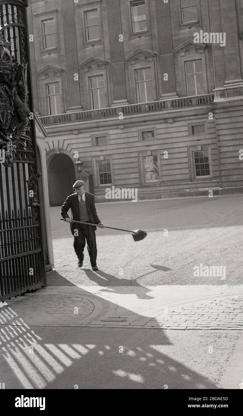 1960s, historical, Buckingham Palace, London, gates open and male worker wearing a suit, sweater and cap, with brush in hand, Westminster, London, England, UK. Stock Photo