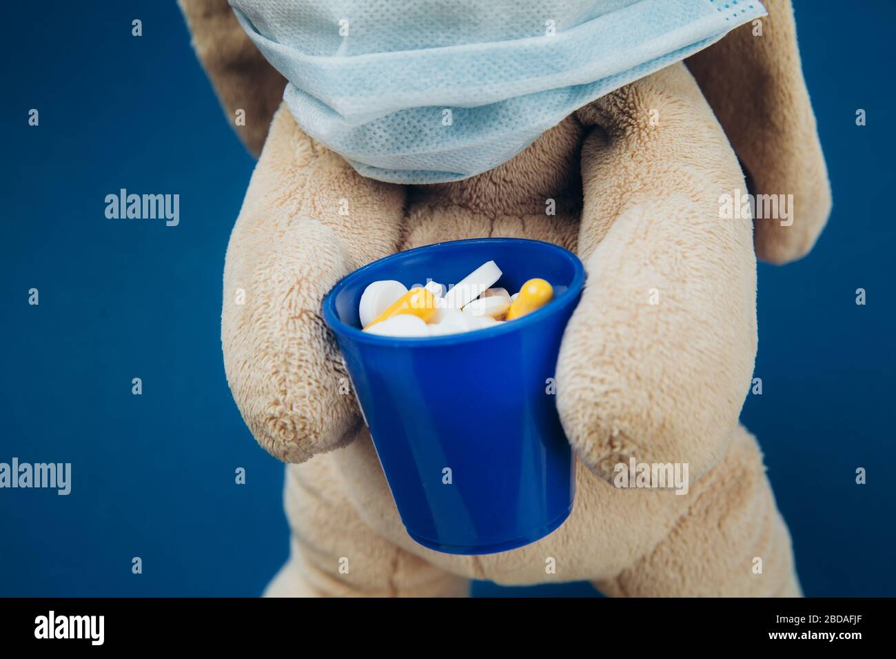 The toy bunny wears a protective medical mask. Flapper holds a glass of pills. Stop coronavirus. Medicine concept. Close up. Stock Photo