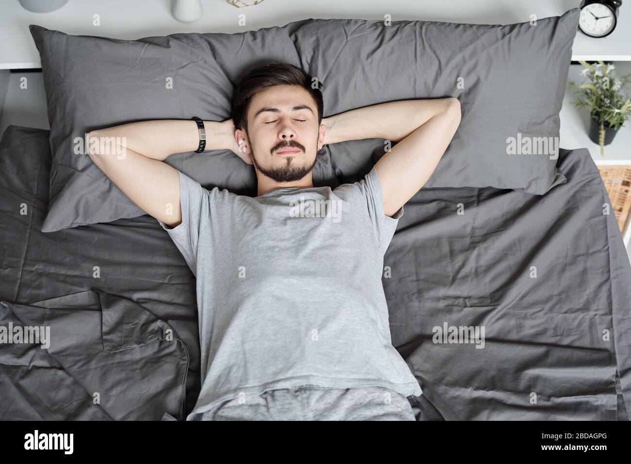 Young bearded man lying with hands behind head while sleeping alone in