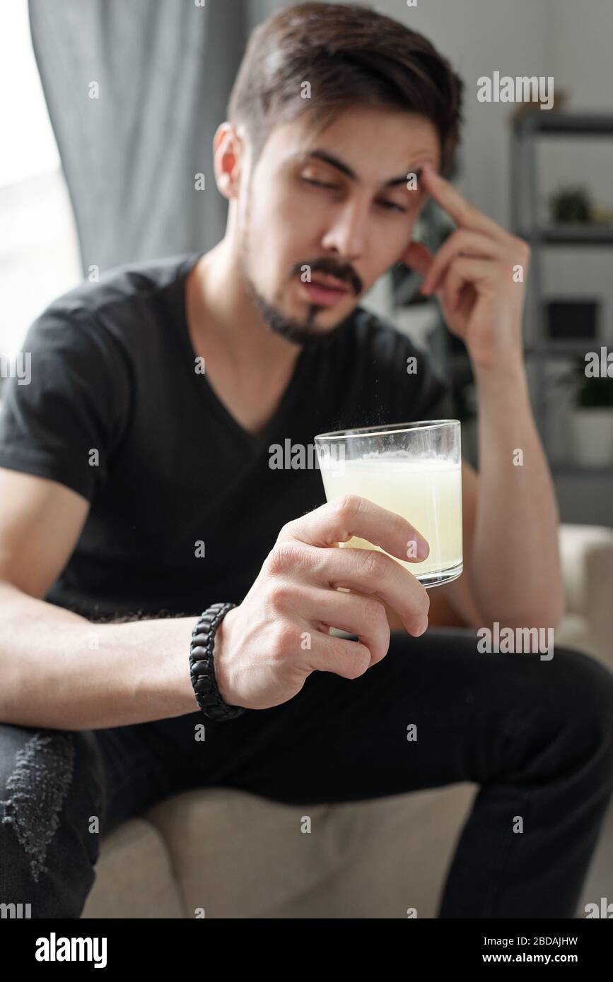 Drunk young man feeling headache in morning after party drinking pill solved in water while curing hangover Stock Photo